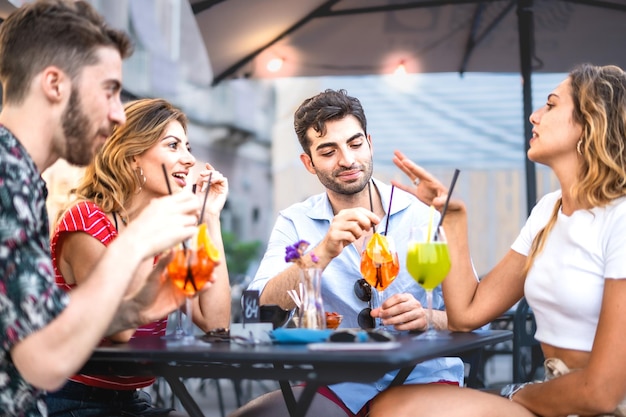 Four trendy young people get together carefree sitting and bonding at outdoors bar restaurant best friends having fun drinking cocktails at summer aperitif life style concept vivid colors