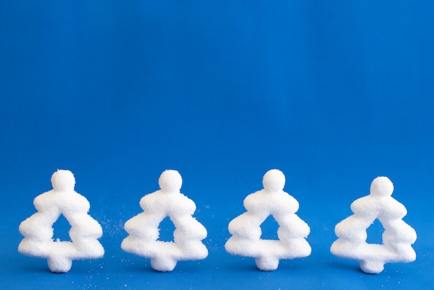 Four white artificial Christmas trees on a blue background