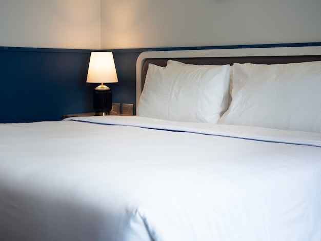 Four white clean pillows blanket and linen bed sheet in the hotel room with copy space Bedding near the lamp in the bedroom