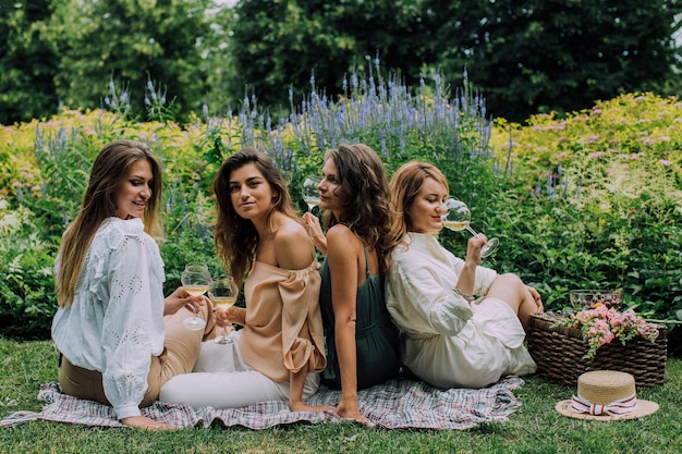 Photo four women sit on a blanket with wine glasses in the grass