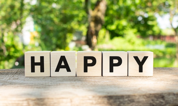 Four wooden blocks lie on a wooden table against the backdrop of a summer garden and create the word...