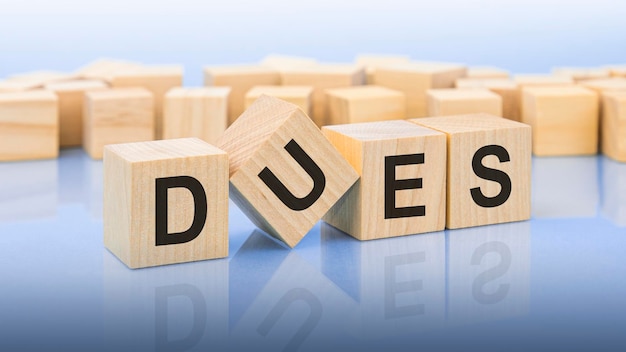 Four wooden blocks with the letters DUES on the bright surface of a blue background the inscription on the cubes is reflected from the surface business concept