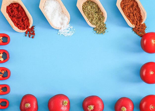 Four wooden small spatulas with hot spices and a frame of cherry tomato radish and chili pepper slices