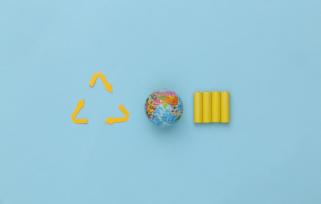 Four yellow AA batteries with recycled arrows sign, globe on blue background. Eco, save planet concept. Top view