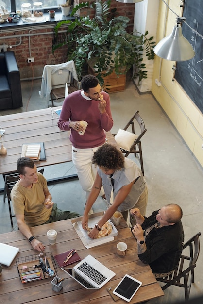 Four young coworkers gathered by table for lunch break