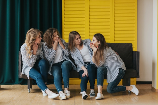 Four young girls in striped shirts, jeans and sneakers posing on the couch. studio shooting.