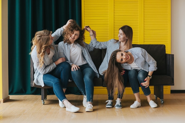 Four young girls in striped shirts, jeans and sneakers posing on the couch. studio shooting.