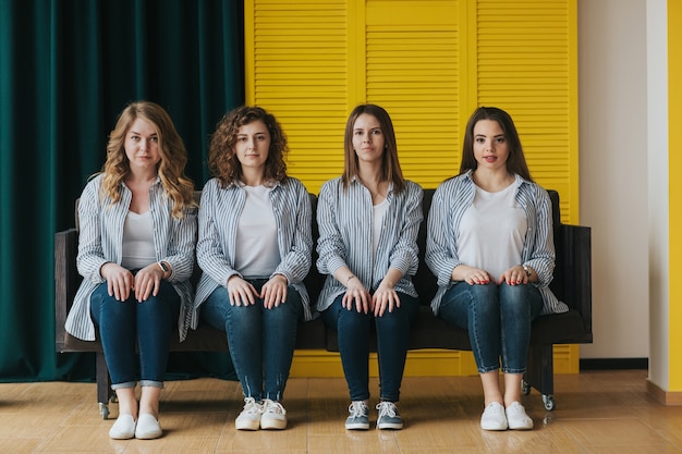 Four young girls in striped shirts, jeans and sneakers posing on the couch