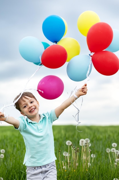 Fouryearold boy with balloons walks in a green meadow with dandelions