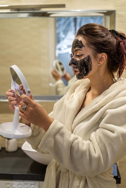 Fragile lady puts a healing black mask on her face to improve her skin