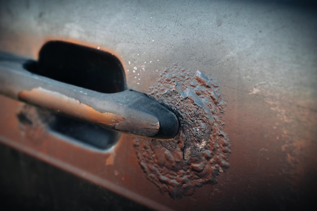 A fragment of the body of a rusty car door with a handle Aggressive corrosion Selective focus