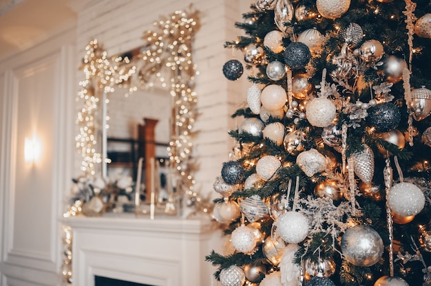 A fragment of a Christmas decorated tree in warm golden colors on a brurred white classic room interior