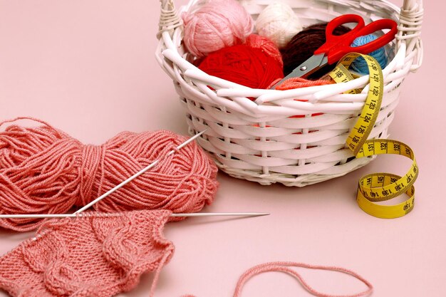 fragment of knitting with a pattern on knitting needles next to basket with multicolored balls of thread