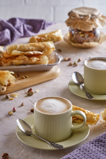 Fragrant cappuccino coffee with puff tubes with meringue and pistachios close-up