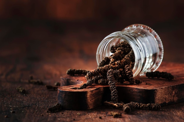 Fragrant long pepper spilling out of glass jar vintage kitchen table background selective focus