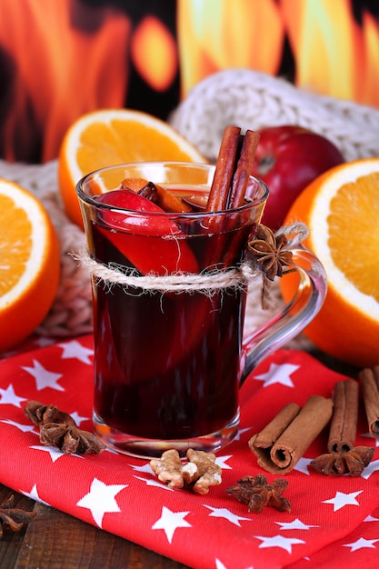 Fragrant mulled wine in glass on napkin on fire background