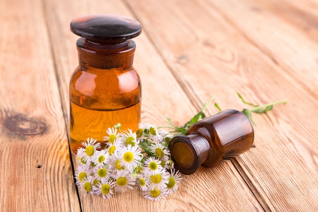 Fragrant oil in a glass bottle with camomile flowers on wooden table