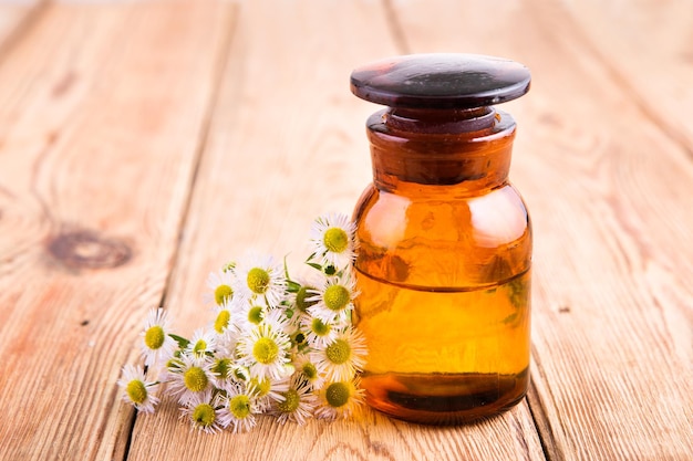 Fragrant oil in a glass bottle with camomile flowers on wooden table