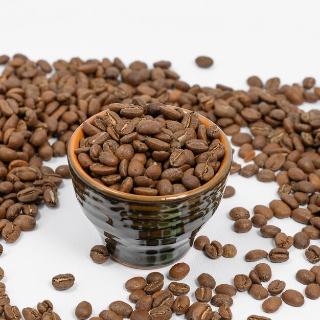 Fragrant roasted coffee beans on a white background and a small cup