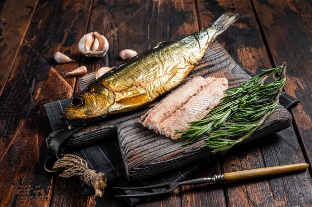 Fragrant Smoked herring fish fillet on wooden board with herbs. Wooden background. Top view.