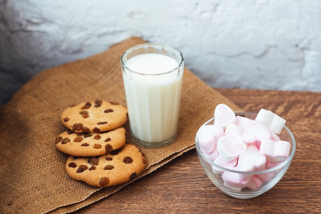 Fragrant tasty homemade cookies with raisins marshmallows in the form of hearts and glass of fresh milk on the table