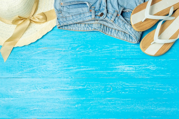 Frame elegant female straw hat slippers jeans on blue wooden background, copyspace, summer vacation.