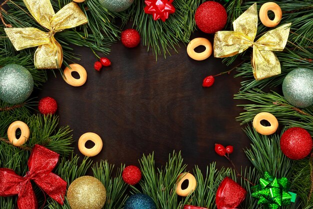 Frame of fir and pine branches bows rose hips Christmas balls and bagels on a wooden background