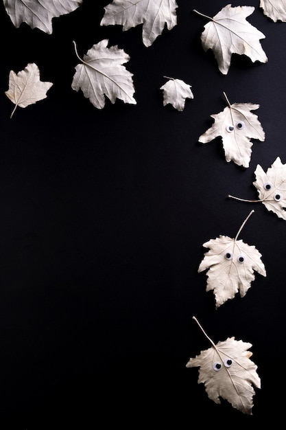 The frame is made of 
autumn leaf with eyes like a ghost  on black  background. Funny Halloween concept. Top view, flat lay