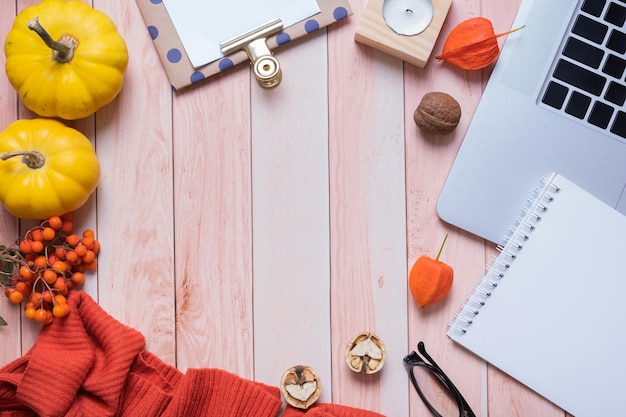 Frame made from note pad laptop sweater and pumpkins on wooden background Autumn cozy decor top view Copy space