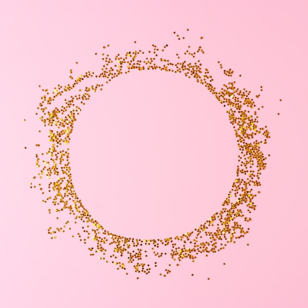 Frame made of golden confetti on pink background