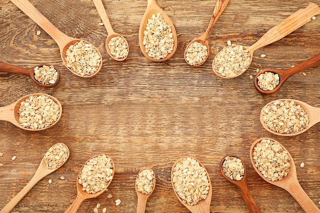 Frame made of spoons with raw oatmeal on wooden background