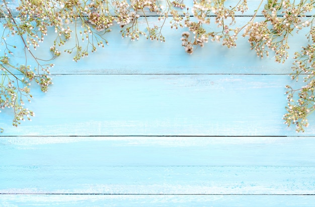 Frame made of white wild flowers on blue wooden background.  