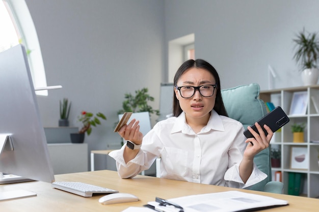 Fraud upset young beautiful asian woman holding phone and credit card a disappointed young lady lost