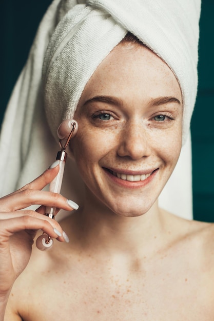 Freckled woman massaging face by jade roller massager after shower beautiful portrait beauty skin cl