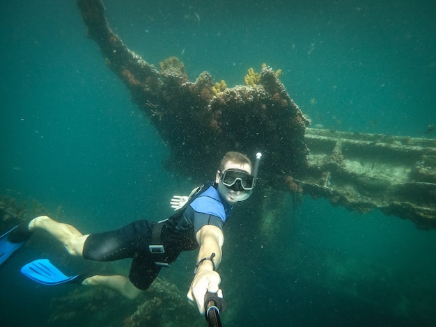 Free diver taking selfie with sunken ship on background.