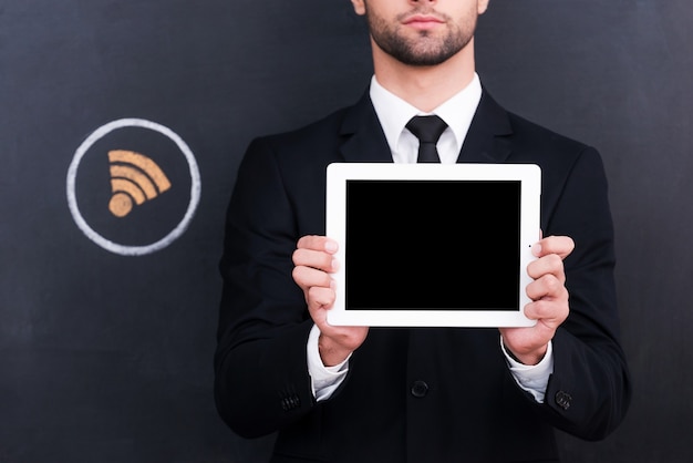 Free Wi-Fi! Close-up of handsome young man holding digital tablet while standing against sharing  symbol chalk drawing on blackboard