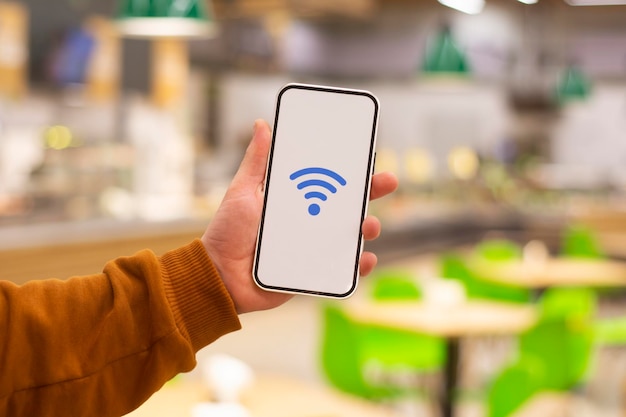 Free WiFi Phone display with wifi icon against the backdrop of a restaurant Man holds a smartphone in his hand closeup