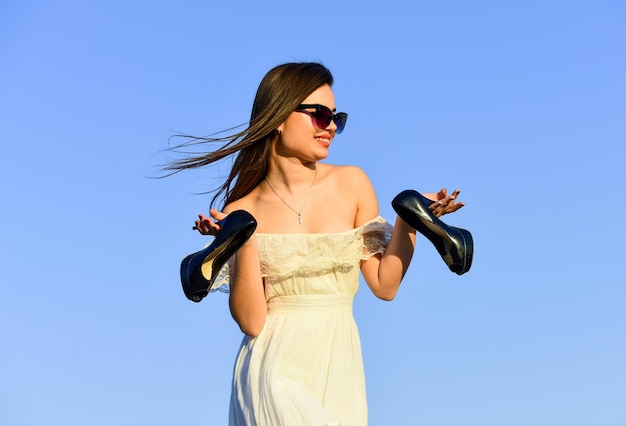 Freedom. Girl in sunglasses copy space. Model tender summer dress. Towards summer. Afterparty concept. Woman sunrise carry high heels in hand. Woman on sunny morning blue sky. Summer holidays.