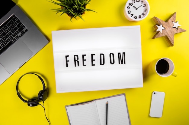 Freedom word on lightbox on modern yellow office desktop with laptop coffee mug