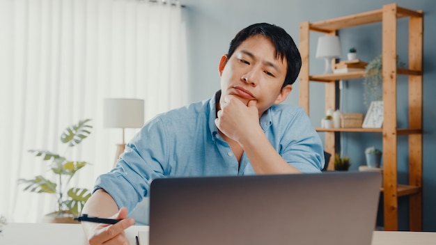 Freelance Asia guy casual wear using laptop online in living room at home office.