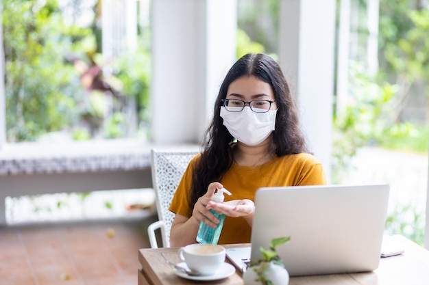 Freelance Business woman using hand put sanitizer on hand for cleaning hand to prevent virus and working with laptop computer with coffee cup and smartphone in coffee shop like the backgroundCOVID19