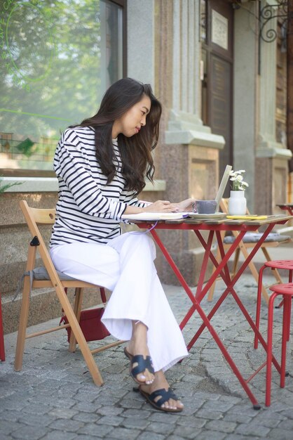 A freelance girl works at a computer in an outdoor cafe