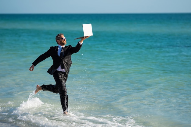 Freelance work online business summer business businessman in suit hold laptop and run on sea funny