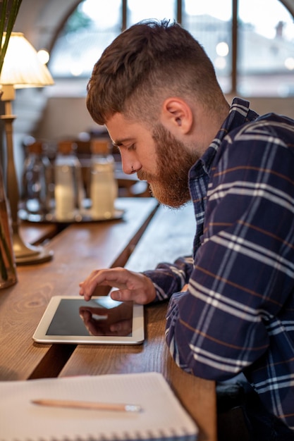 Freelancer dressed in casual outfit focus on reading news and looking on digital tablet while sittin...