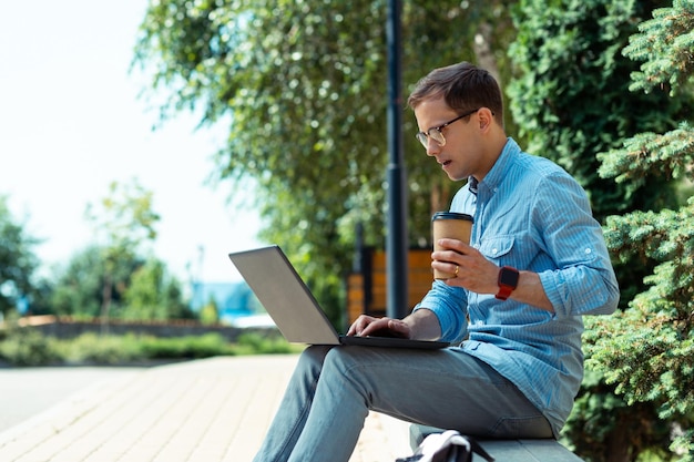 Freelancer drinking takeaway coffee and working on laptop outside