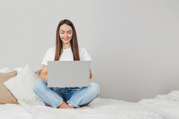 Freelancer girl sits on a bed using laptop looks at the monitor and works