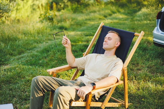 Freelancer man sits on a wooden chair in nature and works online on a laptop A man travels and works remotely on a laptop computer Office work in nature Vacation