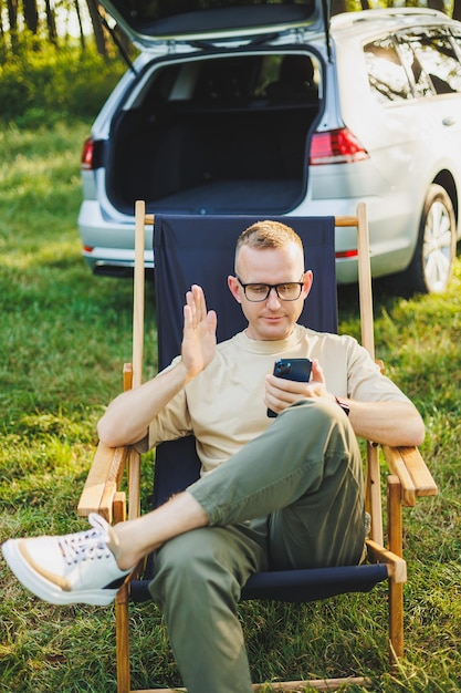 Freelancer man sits on a wooden chair in nature and works online on a laptop A man travels and works remotely on a laptop computer Office work in nature Vacation