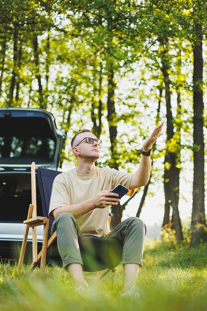 Freelancer man sits on a wooden chair in nature and works online on a laptop A man travels and works remotely on a laptop computer Office work in nature Vacation