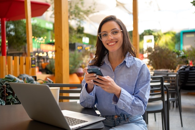 Freelancer using smartphone and laptop sitting outdoor cafe